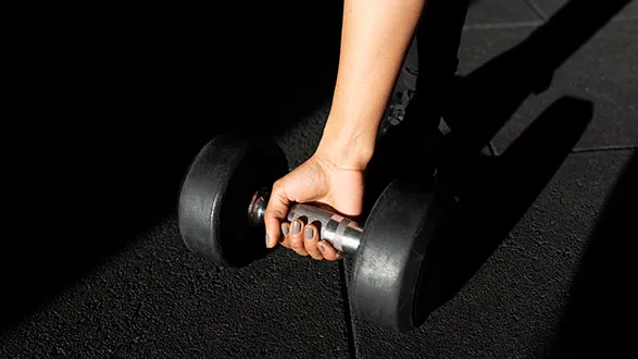 A hand picking up dumbbell from floor to rerack weight